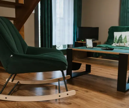 Grafika Stylowy salon z zielonym fotelem bujanym, sofą, stolikiem kawowym i drewnianymi schodami.