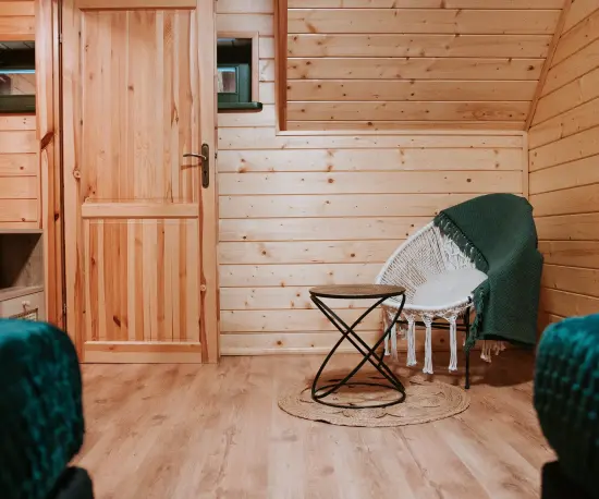 Grafika Jasne drewniane wnętrze z zielonymi akcentami i przytulnym fotelem.