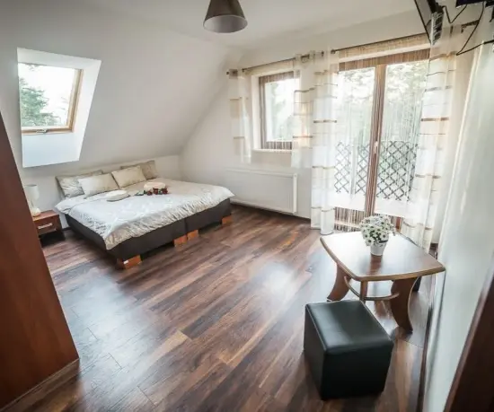 Grafika Jasny pokój na poddaszu z łóżkiem, oknami i małym stolikiem hotel Dolce Vita
